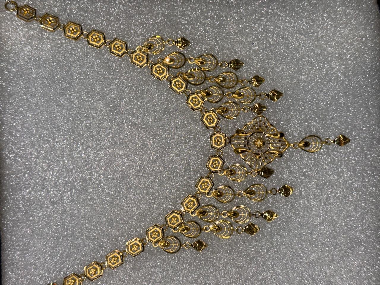 A gold necklace with hexagonal links and tassel drops, laid flat